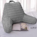 Gray backrest pillow on a bed with an open book and glasses nearby