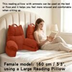 A woman sits on a bed reading a book, supported by two rust-orange ribbed reading pillows with armrests. The scene is a softly lit bedroom with a cream upholstered headboard, white bedding, and text describing the product and its use.